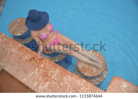 A girl in a bikini sits in a pool and tries a red wine