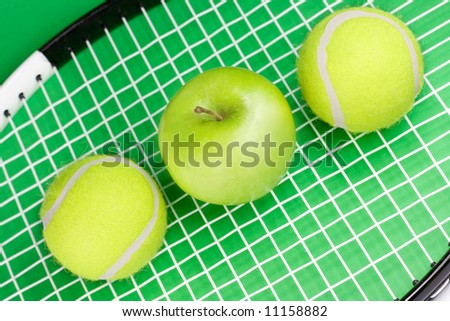 Two tennis balls with apple and racket on green background