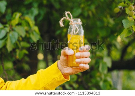 a bottle of orange juice in a hand. mango juice in a transparent glass bottle. summer vivid photo in the garden on the background of leaves and greens
