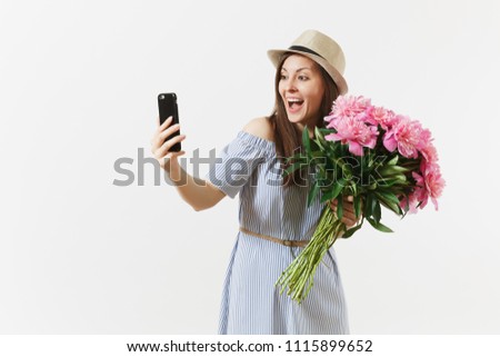 Young woman in blue dress, hat holding bouquet of beautiful pink peonies flowers, doing selfie on mobile phone isolated on white background. St. Valentine's, International Women's Day holiday concept