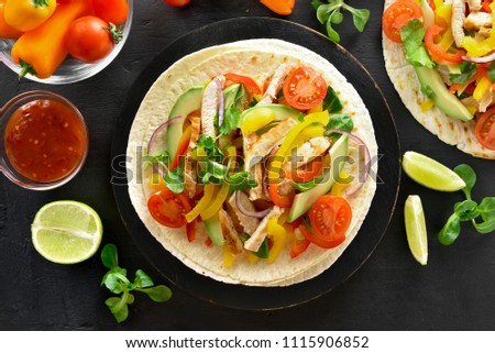 Tacos with grilled chicken meat and vegetables on black background. Top view, flat lay