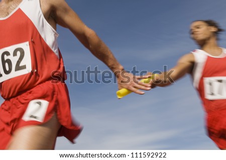Male athletes passing baton in relay race Royalty-Free Stock Photo #111592922