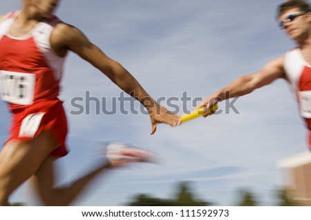 Blurred motion male runners passing baton in relay race Royalty-Free Stock Photo #111592973