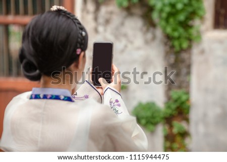 Woman wearing Hanbok, Korean traditional dress costume and taking photo with cell telephone or smartphone digital camera for Post Online on the Internet at walk and travel in Seoul city, South Korea