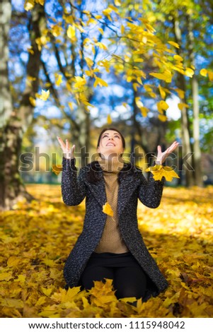 young beautiful woman playing with autumn leaves in park