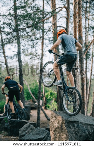 athletic young trial bikers performing stunts on boulders