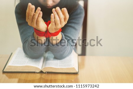 Hands female prayer to God on the bible but her hands tied up with rope,Concept Pray for liberation,sin,no freedom.