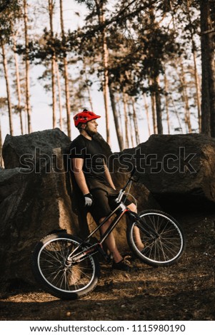 young trial biker leaning back on rocks outdoors in forest