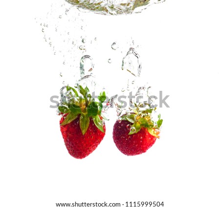 Red strawberries dropped into the water with splash on a white background