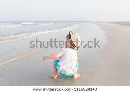 Little kid boy looking at the blue sea on the tropical beach at summer vacation at sunny day, he smiling and feels happy