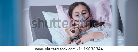 Sick young girl in a hospital bed sleeping with an oxygen mask and a toy, getting treatment for cystic fibrosis Royalty-Free Stock Photo #1116036344