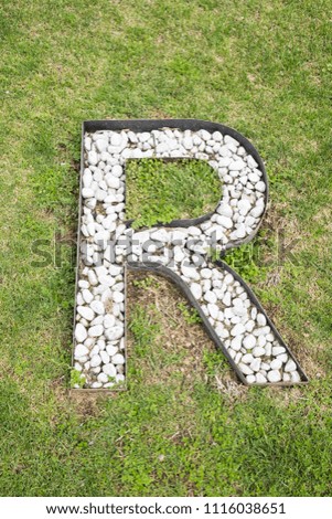 Letter R built from white stones on green grass as seen from high above