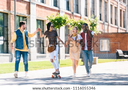 happy multiracial friends with long board having fun while spending time together on street