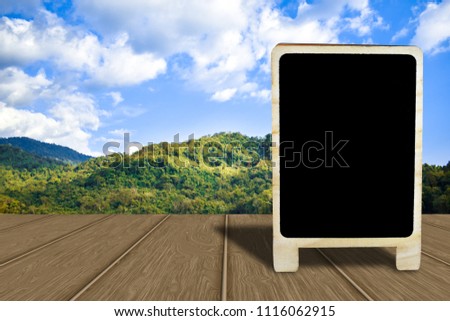 black empty chalkboard standing on wood table with nature background, sky and mountain background, Mock up for display or montage of product or design
