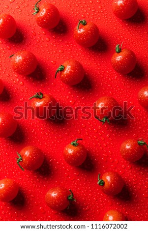 top view of pattern of cherry tomatoes on red surface with water drops