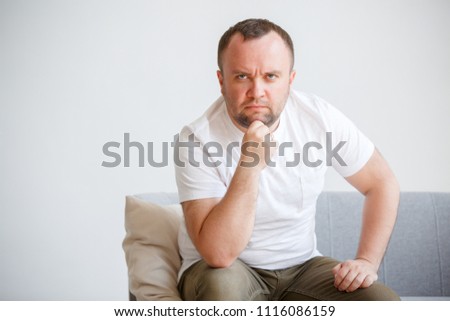 Image of man in white T-shirt sitting on sofa