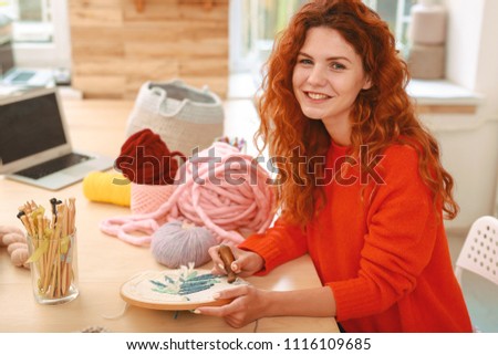 Freelancer on break. Happy beaming freelancer embroidering nice floral picture during her lunch break