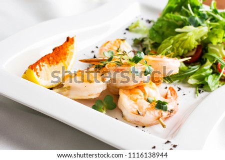 Tiger prawns on skewers with lemon and greens on a white dish
