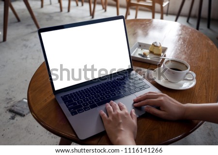 Mockup image of hands using laptop with blank white desktop screen with coffee cup and cake on wooden table in cafe