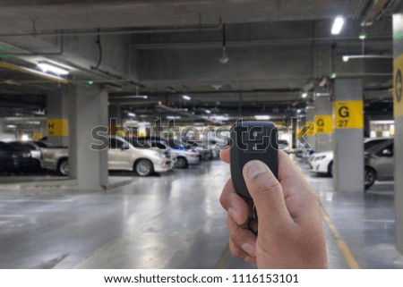 Male holding car keys remote with car on Parking garage In the mall for background.