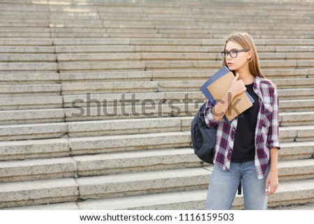 Attractive serious student girl with books on university stairs background, looking away, dreaming or thinking during break, having rest in campus. Education concept, copy space