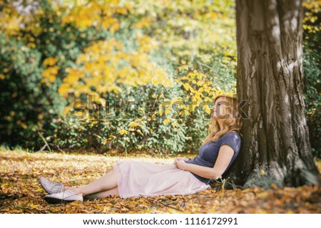 young blond hair woman sit under tree in autumn park and dreaming	