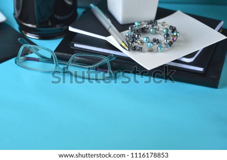 Turquoise blue styled desktop with black and white stationery, optical glasses and blank copy space. Working from home office. Studying, freelancing and creative business concept.