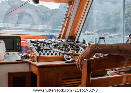 Navigation console with metal steering wheel inside the motorboat deck house. Boat driver sitting near the wheel. Dirty windows splashing with sea water.  Royalty-Free Stock Photo #1116198293