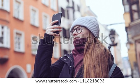 A young woman in scarf taking a picture in the old streets of Europe