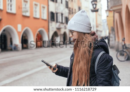 A young woman in scarf taking a picture in the old streets of Europe