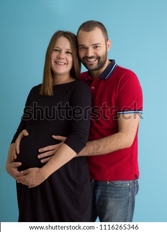 Portrait of a happy young couple,man holding his pregnant wife belly isolated over blue background