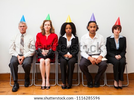 A group of office workers looking bored or disinterested while wearing party hats. Humorous business concept.