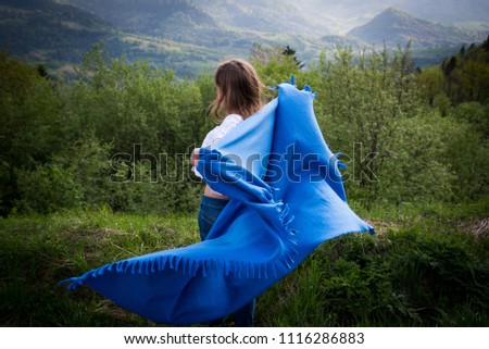 Girl travel in mountains alone. Spring weather, calm scene. view over landscape in sunlight. Wanderlust photo series. View from the back. The Carpathians mountains. Wearing poncho.