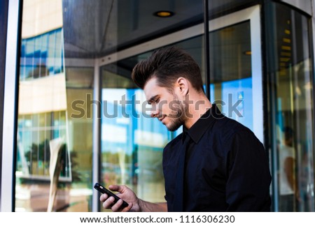 Confident man skilled office worker reading text message on mobile phone, standing near business centre. Successful male financier checking e-mail in internet via cellphone, standing outside company 