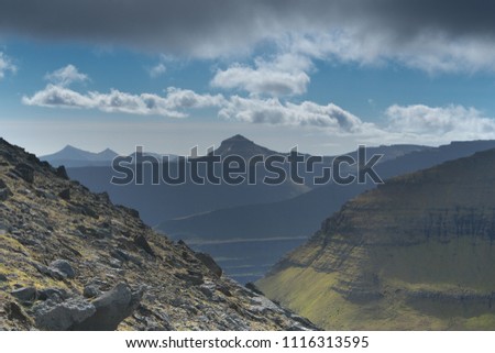 Scenic landscape with perspective view to the majestic mountains showing the effect of erosion, rocks, grass, blue sky, dark clouds in the Faroe Islands. Colourful travel background.