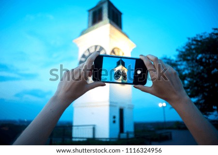 Girl taking a photo of the tower clock on her mobile phone. Shallow depth of field.