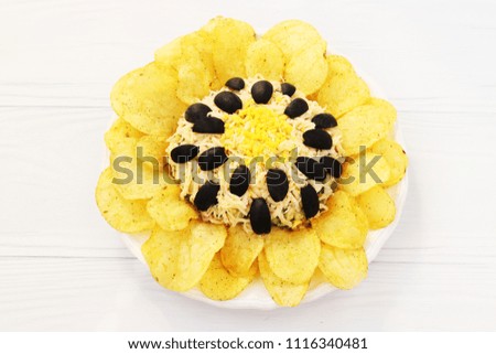 Salad in the form of sunflower, decorated with potato chips located on a plate on a white background