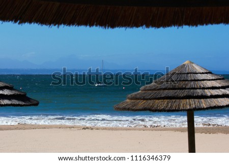 Palapas On The Beach With Sailing Boat At Anchor