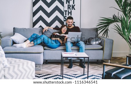 Young marriage resting on comfortable couch and watching funny movie on modern laptop device using wireless home internet.Couple in love doing shopping online together on digital netbook in apartment Royalty-Free Stock Photo #1116346541