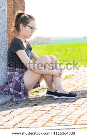 Young Asian female sitting on a concrete column in a park.
