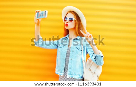 Pretty girl takes a picture self portrait on a smartphone on orange background