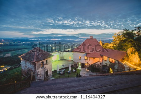 Night time panorama of a castle on a hill looking towards the wide plains and fields of Drava region in Vurberg, Maribor, Slovenia during a picturesque summer sunset.