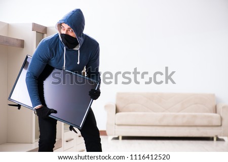 Man burglar stealing tv set from house Royalty-Free Stock Photo #1116412520