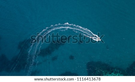Aerial view of a white motorboat running on the azure waters of the Tyrrhenian Sea. On his trip near the coast the boat leaves a white trail in the waves of the sea. Royalty-Free Stock Photo #1116413678