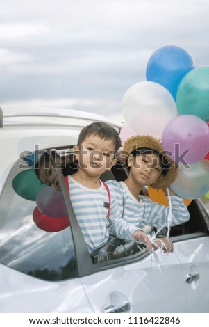 Happy family holding colorful balloons outdoor on the car having great holidays time on summer. Lifestyle, vacation, happiness, joy concept