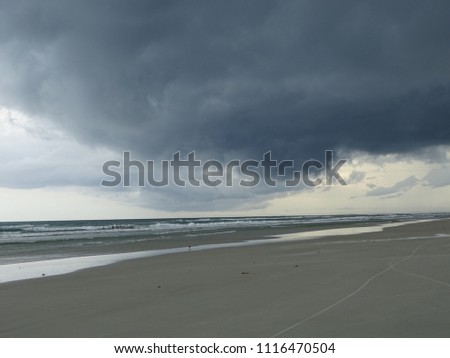 Beautiful beach waves surf horizon, turquoise blue reflecting water and storm clouds in gray sky.