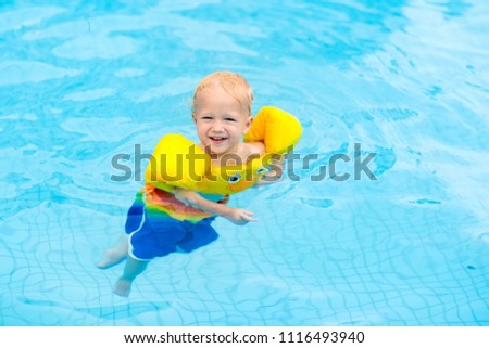 Baby with inflatable armbands in swimming pool. Little boy learning to swim in outdoor pool of tropical resort. Swimming with kids. Healthy sport activity for children. Summer vacation. Swim aids.