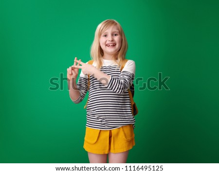 smiling school girl with backpack showing hashtag gesture on green background