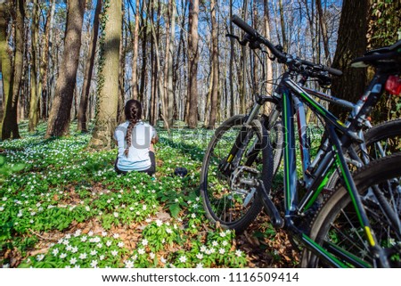 young woman resting in forest in the center of blooming white flowers fields after bicycling