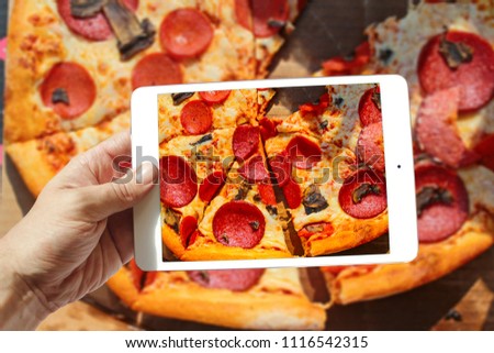 male hand holding tablet take photo of Pepperoni pizza with mushrooms